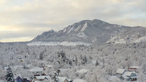 Low-drone-shot-moving-right-of-Boulder-Colorado-and-rocky-Flatiron-mountains-after-large-winter-snow-storm-covers-trees,-homes,-streets,-and-neighborhood-in-fresh-white-snow-for-the-holidays