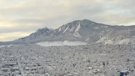 High-wide-drone-shot-moving-forward-of-Boulder-Colorado-and-rocky-Flatiron-mountains-after-large-winter-snow-storm-covers-trees,-homes,-streets,-and-neighborhood-in-fresh-white-snow