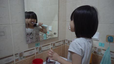 A-Chinese-Indonesian-girl-is-brushing-her-teeth-with-electrical-toothbrush-in-front-of-a-mirror-inside-a-children-friendly-toilet