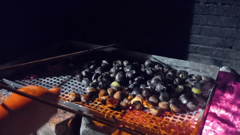 Roasting-chestnuts-over-coals,-a-man's-hand-stirs-the-chestnuts
