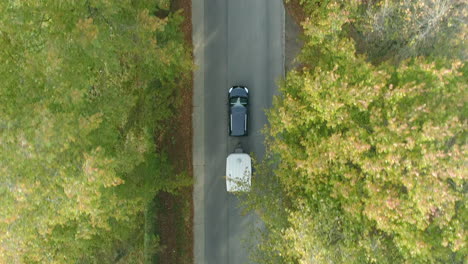 Overhead-View-Of-A-Car-With-Trailer-Driving-In-The-Tree-lined-Road