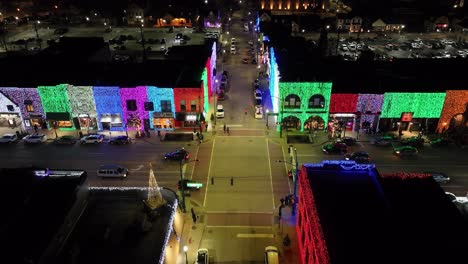 Rochester,-Michigan-street-corner-at-night-lit-up-with-Christmas-lights-on-buildings-along-with-traffic-and-drone-video-stable
