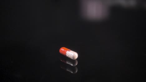 Pill-falling-down-on-a-black-glass-surface,-mirror-surface-with-a-reflection-on-black-background