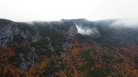 Antenne-Von-Wolken-Und-Nebel,-Die-Während-Der-Herbstsaison-über-Die-Spitze-Einer-Bergklippe-Kommen