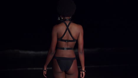 Young-girl-in-a-bikini-walks-towards-to-ocean-waves-at-night-on-a-Caribbean-island