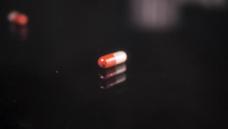 Pills-falling-down-on-a-black-glass-surface,-mirror-surface-with-a-reflection-on-black-background
