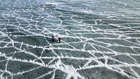 two-fisher-man-waking-on-frozen-lake,-icy-lake-texture,-winter-fishing,-frozen-lake,-Ariel-drone-shot-60fps-Lake-St-Clair-Mitchell's-Bay