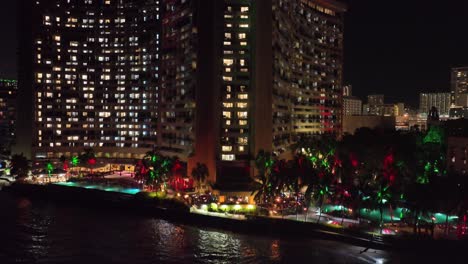 Imágenes-Aéreas-De-Drones-Del-Hotel-Waikiki-Por-La-Noche-Con-Edificios-Brillantes-Y-Mucha-Luz-Con-Tráfico-Y-Palmeras-Oahu-Hawaii-Con-Luces-De-Colores