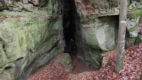 Man-coming-through-Huge-Rock-Formations-in-Mullerthal-Hiking-Trail-in-Luxembourg---Camera-on-front