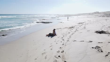 Ein-Romantisches-Paar,-Das-Am-Strand-Sitzt-Und-Sich-über-Dem-Weißen-Sand-Des-Südafrikanischen-Strandes-Küsst---Luftkreisaufnahme