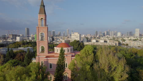 Rosa-Kirche-Umgeben-Von-Bäumen-Und-Der-Skyline-Von-Tel-Aviv-Im-Hintergrund