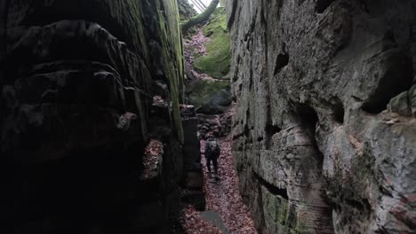 Man-walking-between-Huge-Rock-Formations-in-Mullerthal-Hiking-Trail-in-Luxembourg---Camera-on-back