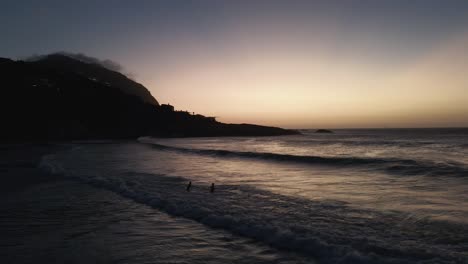 Ein-Paar,-Das-Mit-Großen-Wellen-Auf-Meer-über-Weißen-Sandstränden-Des-Südafrikanischen-Strandes-Spielt,-Sonnenuntergangszeit---Luftaufnahme