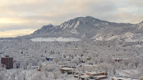 High-drone-shot-moving-left-of-Boulder-Colorado-and-rocky-Flatiron-mountains-after-large-winter-snow-storm-covers-trees,-homes,-streets,-and-neighborhood-in-fresh-white-snow-for-the-holidays