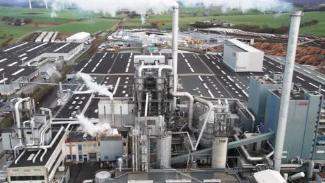 Vista-Aérea-De-Una-Fábrica-De-Procesamiento-De-Madera-Contaminante-En-Alemania:-Humo-Del-Proceso-De-Producción-Que-Llena-La-Atmósfera-En-El-Patio-De-Fabricación-De-La-Planta