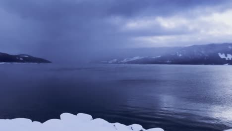 Slow-pan-over-dramatic-dark-moody-Upper-Arrow-Lake-British-Columbia-covered-in-snow-and-revealing-the-ferry-port