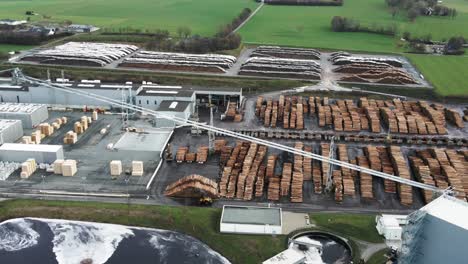 Aerial-View-of-Wood-Processing-Factory-in-Germany-,-Pine-Tree-Wood-Logs-Stacked-in-Rows-and-Heavy-Machinery-on-the-Move-at-the-Site
