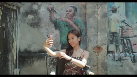 Attraktives-Asiatisches-Mädchen-Macht-Tagsüber-Ein-Selfie,-Das-Vor-Einem-Wandgemälde-In-Chinatown-In-Malaysia-Posiert