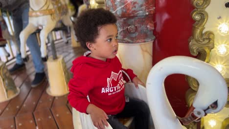 Lovely-twó-year-old-black-baby,-mix-raced-,amazed-on-a-carousel,-wearing-a-red-jacket