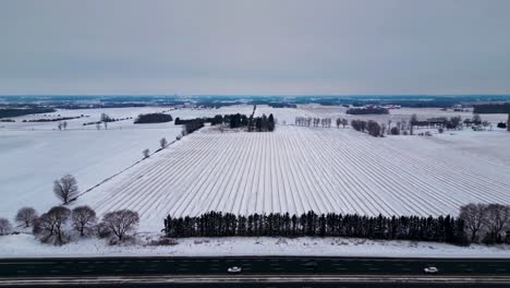 Canada-highway-401-in-winter,-with-farm-in-background-with-snow-covered-field-and-cars-and-truck-traveling