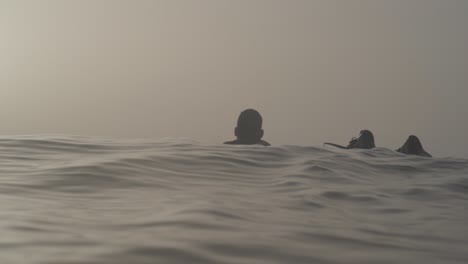 Silhouette-of-male-surfer-paddles-in-the-ocean-during-foggy-morning,-Slow-motion