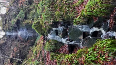 Vertical-shot-of-a-small-waterfall-off-of-a-hiking-trail-in-Scotland