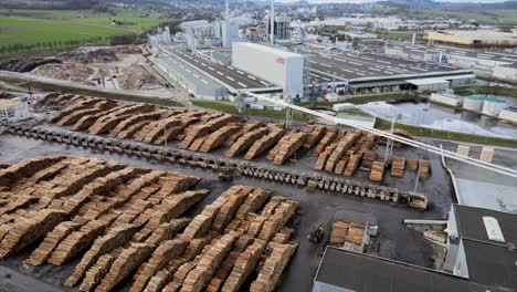 Aerial-Look-at-Wood-Processing-Plant-in-Germany,-Showing-Polluting-Smoke-and-Rows-of-Chopped-Pine-Logs