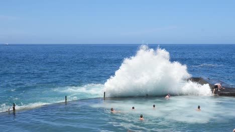 Wave-crashing-over-sea-wall-into-natural-swimming-pool-pushing-the-swimmers