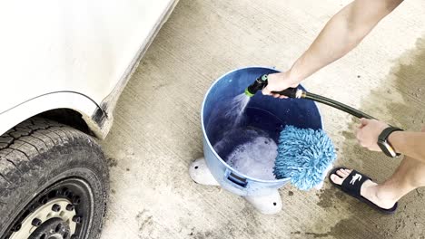 Long-clip-of-a-young-white-male-filling-up-a-blue-bucket-with-soap-and-water-getting-ready-to-wash-a-filthy-muddy-white-car