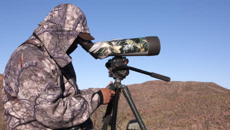 Hunter-using-a-telescope-to-look-for-animals-in-full-camo
