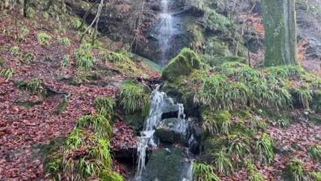 Tilting-upward-shot-of-a-small-waterfall-and-stream-off-of-a-hiking-trail-in-Scotland