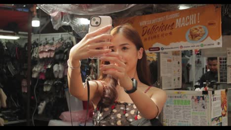 Asian-attractive-girl-takes-a-selfie-posing-in-front-of-stall-in-Malaysia-in-daytime