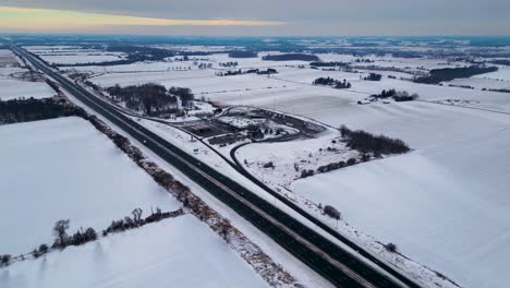 Canada-highway-401-gas-station-covered-in-snow-with-farm-and-field-in-background-60fps-aerial-drone-shot,-winter