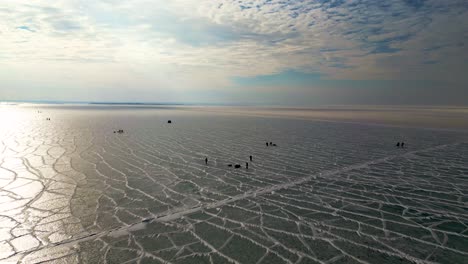 People-fishing-and-walking-on-frozen-lake,-with-blue-sky-and-icy-texture,-Lake-St-Clair-60fps-aerial-drone-shot