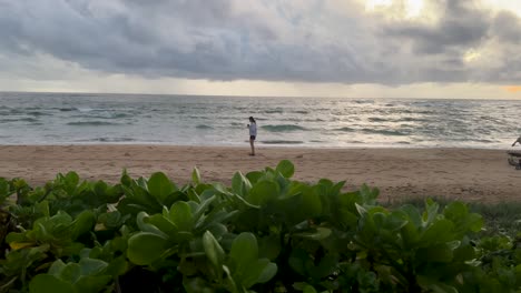 woman-looking-out-at-ocean-turns-around-from-far-away-to-take-picture