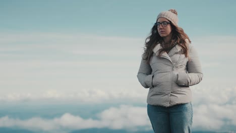 Slow-motion-of-a-young-woman-with-long-brown-hair-and-glasses-standing-on-top-of-a-beautiful-mountain-landscape-on-a-windy-and-cloudy-day