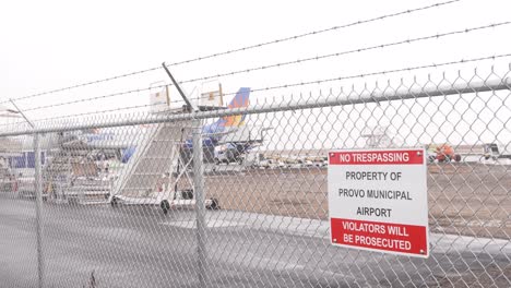 No-Trespassing-sign-on-the-fence-at-Provo-Municipal-Airport-with-a-Allegiant-Airlines-airplane-at-the-departure-or-arrival-gate-on-a-snow,-sleet-and-rain-day
