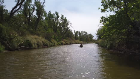Backward-dolly-shot-of-a-family-paddling-upstream-on-a-small-river
