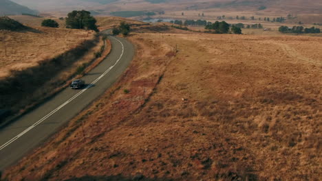 Drone-shot-following-a-black-Austin-Westminster-vintage-car-driving-through-the-hills-of-south-africa-during-dry-winter-4K