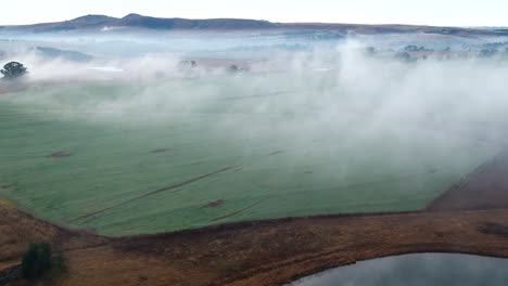 Drone-shot-early-morning-mist-over-green-farmlands-during-dry-winter-conditions-in-South-Africa