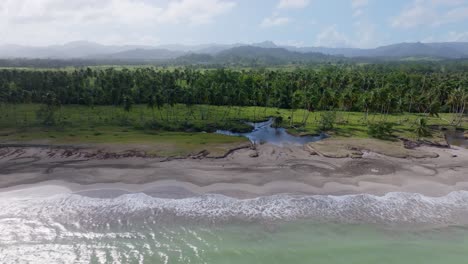 Trucking-drone-shot-of-reaching-water-of-ocean-at-sandy-beach-and-tropical-PLAYA-BAHIA-ESMERALDA,-MICHES