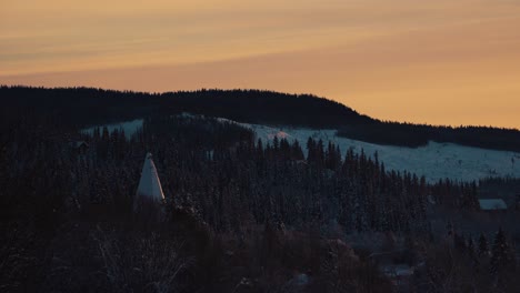 Shot-of-coniferous-trees-along-the-hilly-slope-covered-with-white-snow-in-Beitostolen,-village-in-Oystre-Slidre-Municipality-in-Innlandet-county,Valdres,-Beito,-Norway-with-sunset