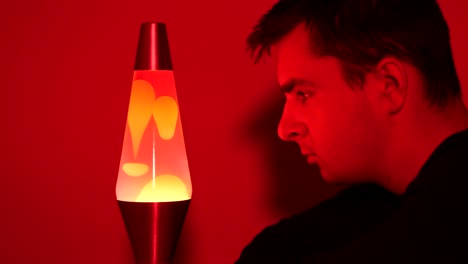 Close-up-of-white-young-adult-male-staring-at-a-red-hot-lava-lamp