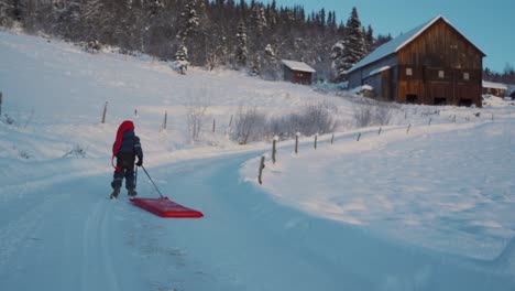 Shot-of-a-little-kid-running-back-along-the-slope-while-having-fun-on-the-snow,-enjoying-sledding-using-red-plastic-shovel-sled-in-Beitostolen,-village-in-Innlandet-county,Valdres,-Beito,-Norway