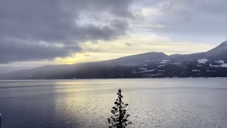 Incredible-reveal-pan-from-behind-a-frost-covered-column-of-Upper-Arrow-Lake,-British-Columbia-at-Halcyon-Hot-Spring-Resort-with-a-beaming-colorful-sunset-over-the-lake-on-a-clear-day