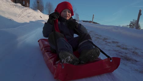 Smiling-Young-Boy-Wearing-Red-Hat-Sledding-Down-During-Christmas-In-Innlandet,-Norway