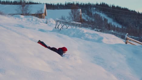Shot-of-a-little-kid-having-fun-on-the-snow,-enjoying-the-pleasures-of-sledding-using-red-plastic-shovel-sled-in-Beitostolen,-village-in-Oystre-Slidre-Municipality-in-Innlandet-county,-Beito,-Norway
