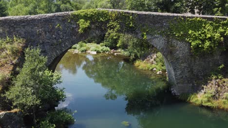 An-ancient-Roman-bridge-in-rural-Spain-over-a-river---drone-flight-under-the-bridge