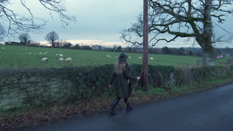 Woman-walking-past-field-of-sheep-in-countryside