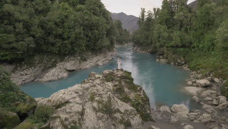 Fairytale-lady-in-dress-standing-on-rock-overlooking-magical-blue-river,-Hokitika-Gorge